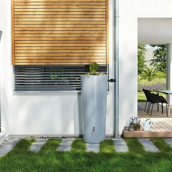 Garantia Modern Line Regenspeicher Stone 2 in 1 - 350 l, Silver - Ein schlanker, grauer Regenspeicher neben einem Fallrohr vor einer modernen Hauswand mit Holzverkleidung und Fenster.