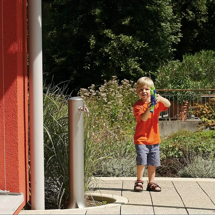 Garantia Wasserzapfstelle Rondo - Sandstein, Höhe: 90 cm - Ein kleiner Junge im Freien mit einer Wasserpistole in der Hand, der an einem sonnigen Tag Spaß hat.
