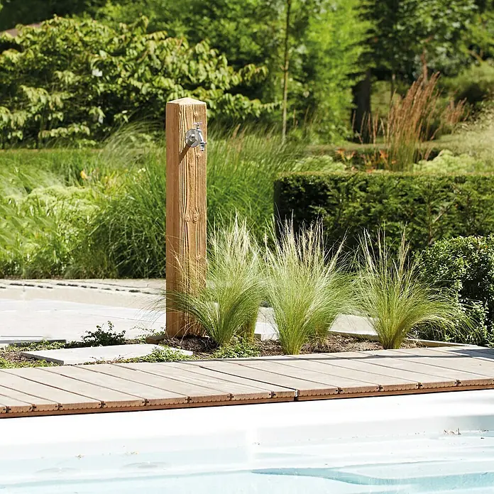 Garantia Wasserzapfstelle Wood - Lightwood, Höhe: 100 cm - Ein rustikaler Wasserhahn aus Holz im Garten, umgeben von Ziergräsern und hellen Holzdielen. Perfekt für die Gartengestaltung.