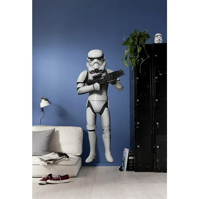 Komar Star Wars Wandtattoo Stormtrooper - 4 -tlg., B x H: 70 x 100 cm - Ein lebensgroßer Star Wars Sturmtruppler mit Blaster-Gewehr in einem modernen Wohnzimmer vor einer blauen Wand.