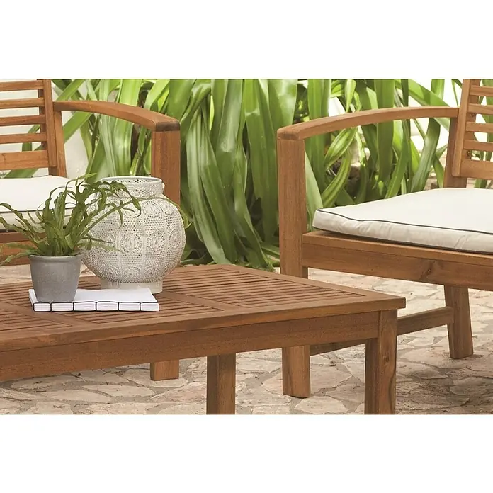 Acamp Loungemöbel-Set Kreta - 4 -tlg., Akazie, Polyester, Braun - Nahaufnahme von Gartenmöbeln aus Holz mit Tisch, Stühlen, Kissen, Vase, Pflanze und Notizbuch auf einem Steinboden mit Pflanzen im Hintergrund.