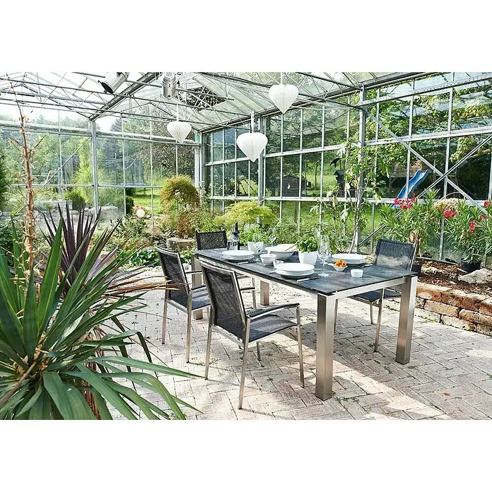 Acamp Gartenmöbel-Set Auris - 7 -tlg., Stapelbar, Silber/Schwarz - Ein stilvoller Esstisch mit vier Stühlen in einem üppigen Gewächshaus, ideal für Mahlzeiten im Grünen.
