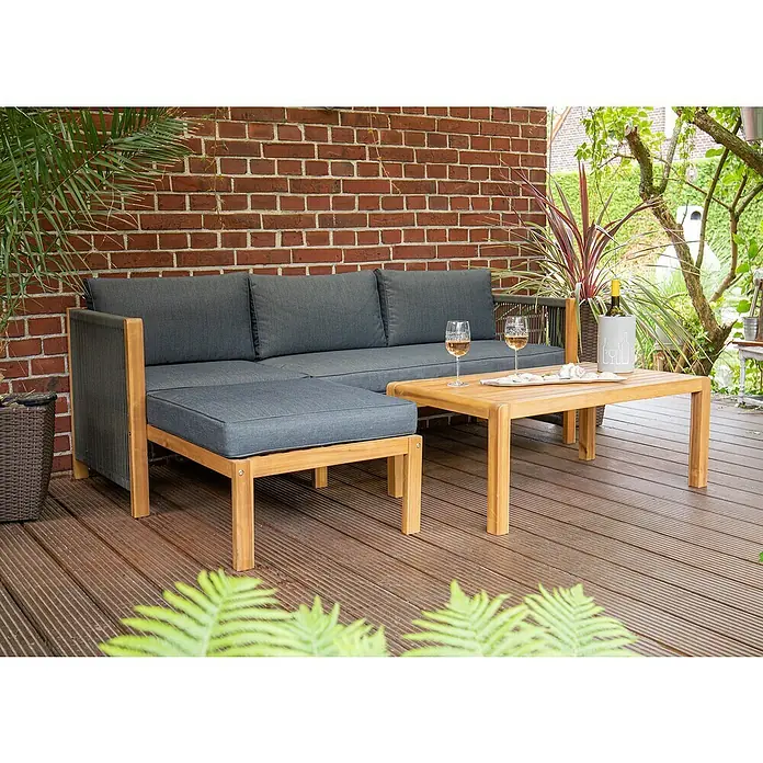 Acamp Loungemöbel-Set Malaga - 3 -tlg., Akazie, Polyester, Braun - Gartenmöbel-Set mit grauem Sofa, Ottomane und Holztisch mit Wein und Gläsern auf einer Terrasse.
