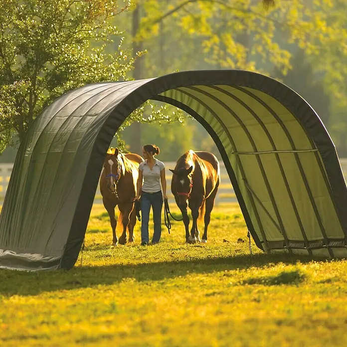 ShelterLogic Garage - Außenmaß inkl. Dachüberstand (B x T): 370 x 610 cm, Kunststoff, Grün - Ein vielseitiges Weidezelt für Pferde, das Schutz vor Sonne und Regen bietet, während eine Frau zwei Pferde hindurchführt.