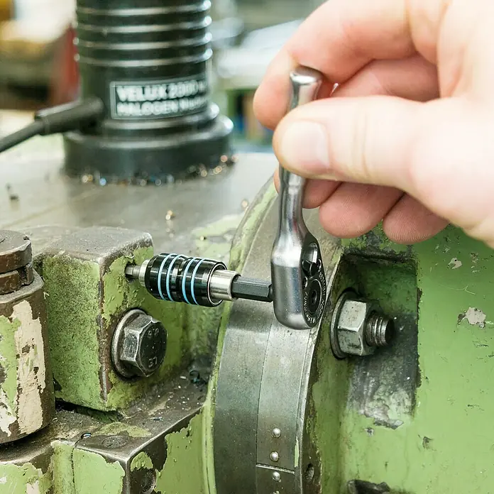 Hazet Umschaltknarre 863 MBIT - Antriebsgröße: ¼″ Sechskant, 89 mm - Eine Hand bedient eine Mini-Ratschenschlüssel mit einem Bit-Halter-Aufsatz an einer Werkzeugmaschine. Fokus auf das Werkzeug.