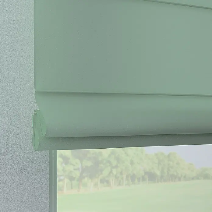 Dekoria Raffrollo -  - Nahaufnahme eines hellgrünen Faltrollos vor einem Fenster, das eine verschwommene Aussicht auf Bäume und eine Wiese bietet.
