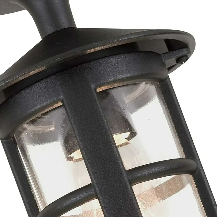 Elstead Außenwandleuchte Hereford - 60 W, 15 x 15 x 23,5 cm, Schwarz, IP23 - Nahaufnahme einer schwarzen Außenleuchte mit klarem Glas und dekorativem Rahmen, die ein warmes Licht ausstrahlt.