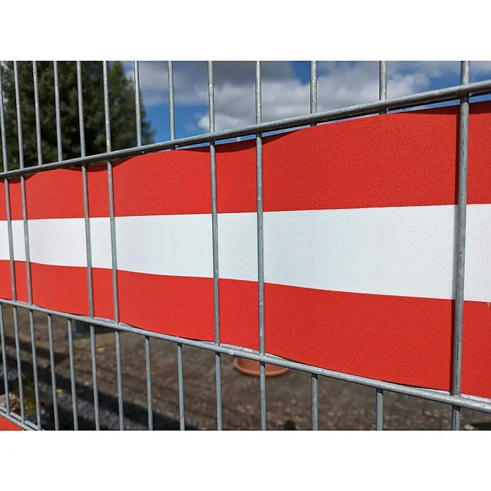 zaun|zu Sichtschutzstreifen Akzentstreifen Österreich - 2,55 m x 0,1 cm x 19 cm, Rot/Weiß, Österreich, Schmal - Rotes und weißes Warnband, das an einem Metallzaun befestigt ist und einen auffälligen Hinweis auf eine Gefahrenstelle gibt.