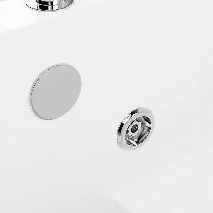 Home Deluxe Badewanne VITAL L - Weiß - Das Bild zeigt einen glänzenden, runden Waschbeckenstöpsel aus Chrom neben einem Ablauf in einem weißen Waschbecken.