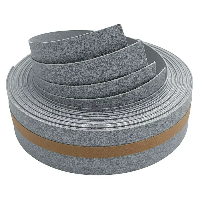 zaun|zu Sichtschutzstreifen Premium 1/4 Set - 2,55 m x 4,7 cm x 0,1 cm, Fenstergrau - Nahaufnahme einer Rolle grauen Kantenumleimers mit einer Klebefläche. Ideal für saubere Kantenabschlüsse im Möbelbau.