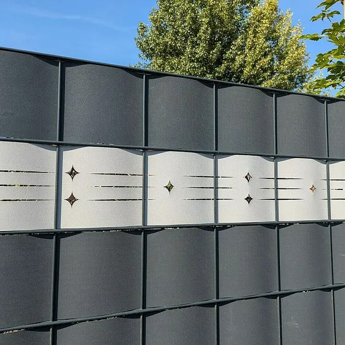 zaun|zu Sichtschutzstreifen Starline Laser - 2,55 m x 19 cm x 0,1 cm, Bordeauxrot - Nahaufnahme eines modernen Zauns mit grauen und weißen Elementen, verziert mit Sternen und horizontalen Schlitzen.