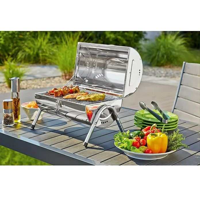 Grillstar Holzkohlegrill DallasGrillfläche (B x T): 34 x 22 cm, Silber - Tragbarer Grill auf einem Tisch im Freien mit Gemüse, Gewürzen und grünem Geschirr. Ideal für Picknicks und Camping.