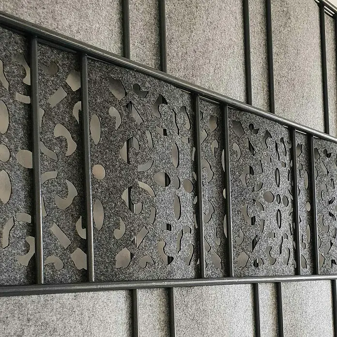 zaun|zu Sichtschutzstreifen Ornament - 2,6 m x 19 cm x 0,2 cm, Anthrazit - Detailaufnahme einer Trennwand mit abstraktem Lochmuster hinter einem Metallgitter, das für ein modernes und luftiges Design sorgt.