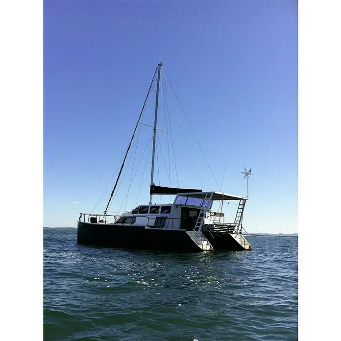 Sunset Windgenerator WG914 - 12 V, Max. Leistung: 300 W - Ansicht eines Katamarans mit Segel und Windgenerator, der auf dem Wasser treibt, vor einem klaren, blauen Himmel.