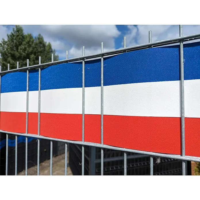 zaun|zu Sichtschutzstreifen Frankreich - 2,55 m x 19 cm x 0,1 cm, Blau/Weiß/Rot, Schmal - Das Bild zeigt einen Zaun mit einer blau-weiß-roten Abdeckung, die an die russische Flagge erinnert, vor einem bewölkten Himmel und Bäumen.