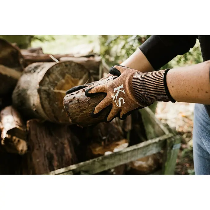 Kent & Stowe Gartenhandschuhe Sure & Grip - M, Braun/Schwarz - Nahaufnahme von Händen mit KS-Arbeitshandschuhen, die ein Stück Holz halten, vor einem Stapel Holz.