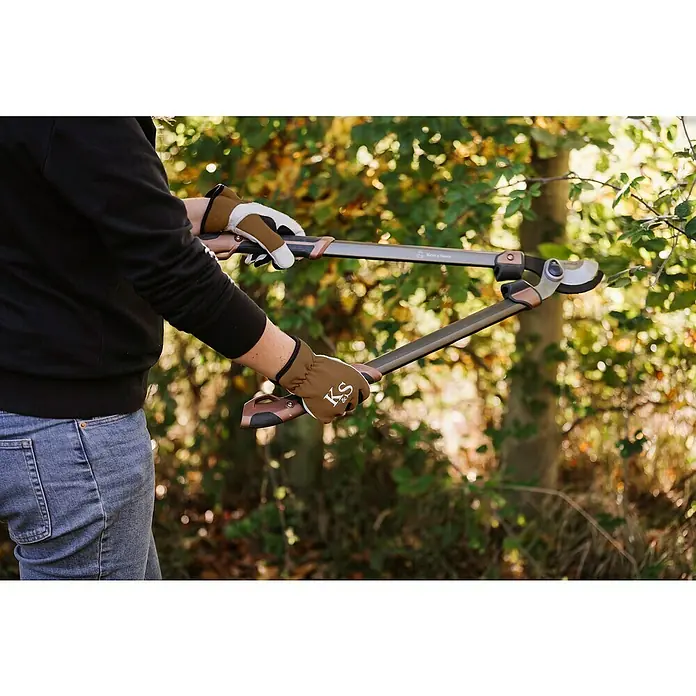 Kent & Stowe Gartenhandschuhe Sure & Fit - L, Braun/Schwarz/Weiß - Eine Person benutzt eine Astschere von Kent & Stowe mit langen Griffen, um Äste zu schneiden, während sie Gartenhandschuhe trägt.