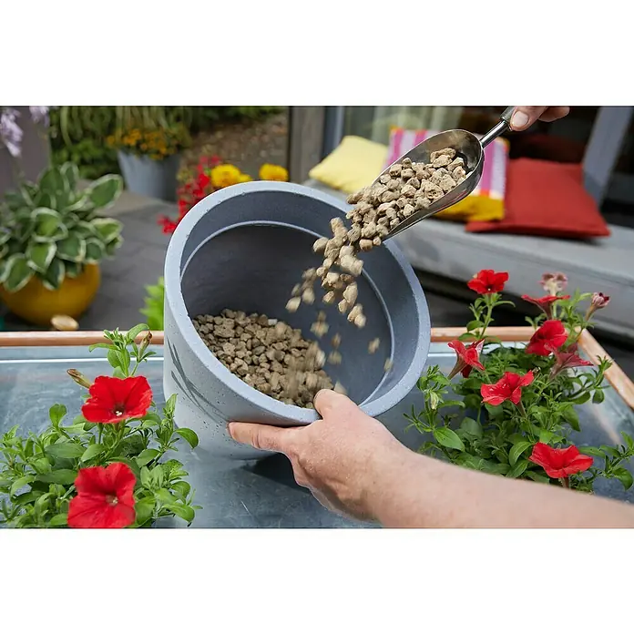 Westland Pflanzgranulat Bims Drainage - 6 l - Eine Person befüllt einen grauen Blumentopf mit Tongranulat, um eine optimale Drainage für die roten Petunien zu gewährleisten.
