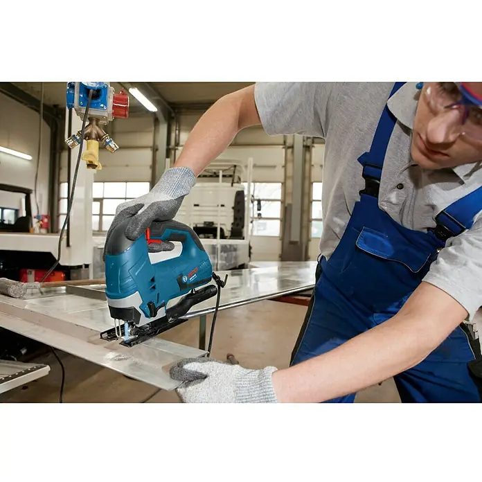 Bosch Professional Elektro-Stichsäge GST 90 BE - 500 /min - 3.100 /min, 90 mm - Ein Handwerker benutzt eine blaue Bosch Stichsäge, um ein Metallstück zu schneiden. Die Stichsäge ist das Hauptprodukt im Bild.