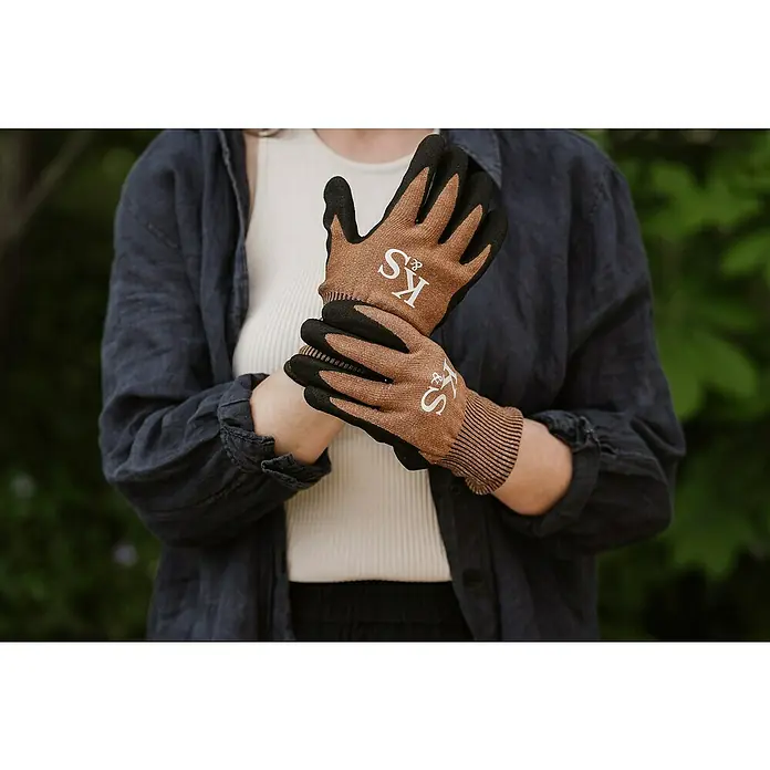 Kent & Stowe Gartenhandschuhe Sure & Grip - M, Braun/Schwarz - Nahaufnahme einer Person, die braune Gartenhandschuhe mit den Initialen KS trägt, die sich ideal für die Gartenarbeit eignen.