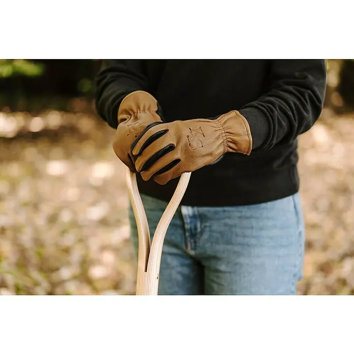 Kent & Stowe Gartenhandschuhe Sure & Soft - S, Braun/Schwarz - Nahaufnahme von Arbeitshandschuhen aus Leder mit Holzgriff einer Schaufel. Ideal für Gartenarbeit und handwerkliche Tätigkeiten.