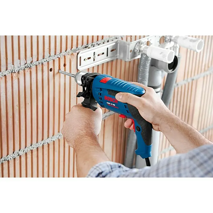 Bosch Professional Schlagbohrmaschine GSB 13 RE - 600 W, Schnellspannbohrfutter - Eine blaue Bosch GSB 13 RE Schlagbohrmaschine wird von einer Person benutzt, um ein Loch in eine Ziegelwand zu bohren.