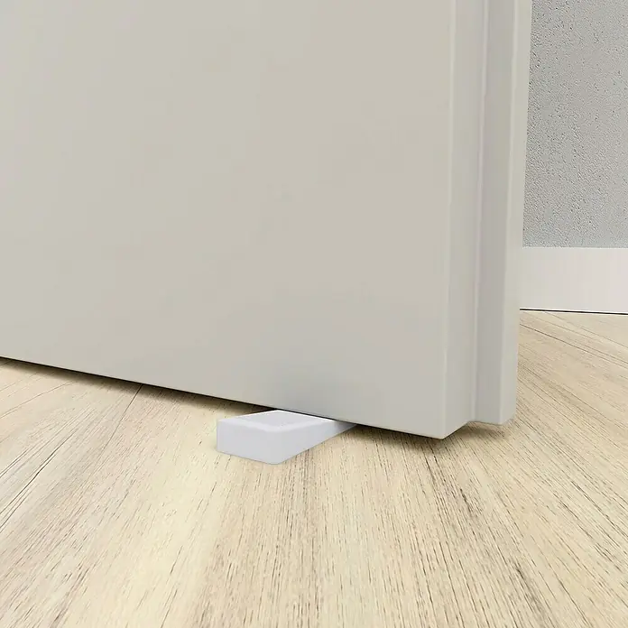 Walteco Türkeil - L x B x H: 15,5 x 50 x 19 mm, Weiß, 4 Stk. - Weißer Türstopper aus Kunststoff unter einer Tür auf einem Holzboden, der verhindert, dass die Tür zufällt.