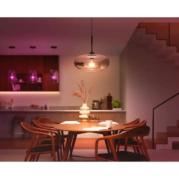 Philips Hue Smart-LED-Lampe White and Color 1100 matter - E27, Dimmbar, RGB, 1.100 lm, 8,1 W - Das Bild zeigt eine moderne Pendelleuchte über einem Esstisch, die eine warme und einladende Atmosphäre schafft.