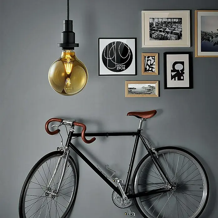 Osram LED-Lampe Vintage Edition 1906 Globe-Form E27 - E27, Nicht Dimmbar, Warmweiß, 410 lm, 4 W, Globe - Ein stilvolles Interieur mit einer Vintage-Glühbirne, die über einem Fahrrad hängt, umgeben von gerahmten Kunstwerken an einer grauen Wand.