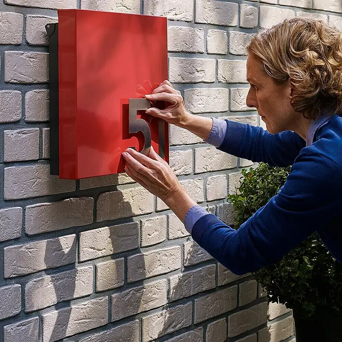 Tesa Montageband - Geeignet für: Mauerwerk, Belastbarkeit pro m: 10 kg, 1,5 m x 19 mm - Frau befestigt Hausnummer "51" an einem roten Briefkasten an einer Backsteinmauer, um die Adresse hervorzuheben.\n