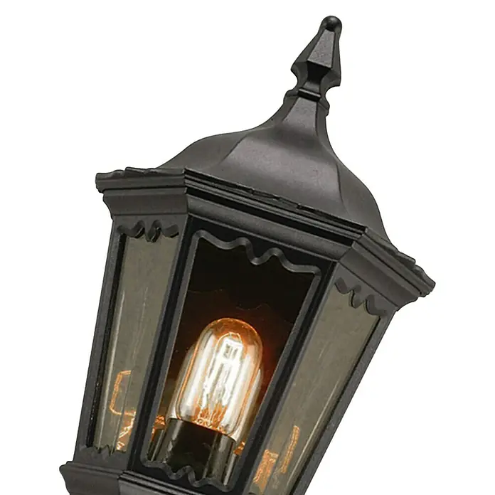 Elstead Außenwandleuchte Medstead - 60 W, 14 x 49,5 x 49,5 cm, Schwarz, IP44, Mit Bewegungsmelder - Nahaufnahme einer dekorativen schwarzen Laterne mit einer glühenden Glühbirne im Inneren, die eine warme und einladende Atmosphäre schafft.