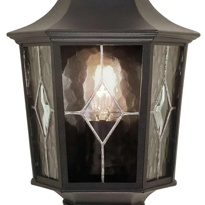 Elstead Außenwandleuchte Norfolk - 60 W, 12,5 x 35,9 x 39,5 cm, Schwarz, IP44 - Nahaufnahme einer schwarzen Außenlaterne mit facettiertem Glas und einer hellen Glühbirne im Inneren, die ein warmes Licht ausstrahlt.