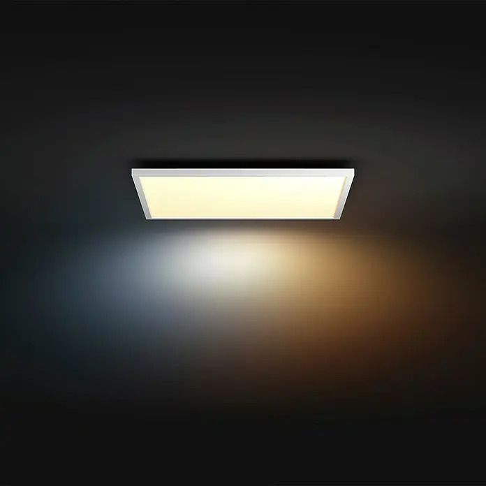Philips Hue LED-Panel White Ambience Aurelle - 39 W, L x B x H: 60 x 60 x 4,6 cm, Weiß, Warmweiß - Eine rechteckige Deckenleuchte mit einem schlanken, weißen Rahmen strahlt ein warmes Licht in einem dunklen Raum aus.