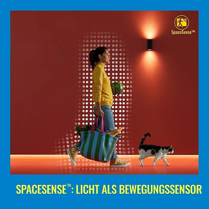 Philips Wiz Smart-LED-Lampe matter - E27, Dimmbar, Neutralweiß, 1.055 lm, 11 W, 1 Stk. - Ein modernes Wandlicht mit Bewegungssensor beleuchtet eine Frau mit Einkaufstasche und eine Katze vor einer roten Wand.