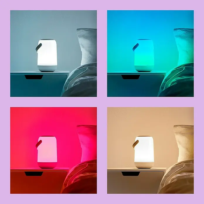 Philips Wiz LED-Tischleuchte Mobile - 14 W, L x B x H: 15 cm x 11,6 cm x 19,3 mm, Weiß, RGB - Vierfeld-Anzeige einer tragbaren Tischleuchte mit veränderbaren Farben, die auf einem Nachttisch neben einem Bett steht.