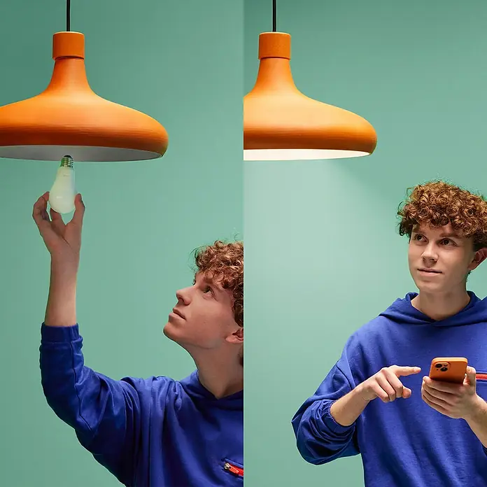 Philips Wiz Smart-LED-Lampe - E27, Dimmbar, RGBW, 12,3 W, 1 Stk. - Das Bild zeigt eine orangefarbene Hängelampe. Auf der linken Seite schraubt eine Person eine Glühbirne ein, während auf der rechten Seite die eingeschaltete Lampe über eine App gesteuert wird.
