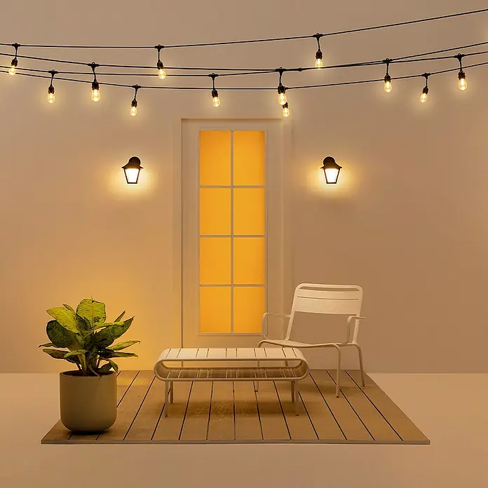 WiZ LED-Außenleuchte Classic - 9,5 W, 22,7 x 17 x 22,8 cm, Schwarz, IP44 - Stimmungsvolle Szene mit Lichterketten, Sesseln und Tisch auf einer Terrasse, die eine gemütliche Atmosphäre ausstrahlt.