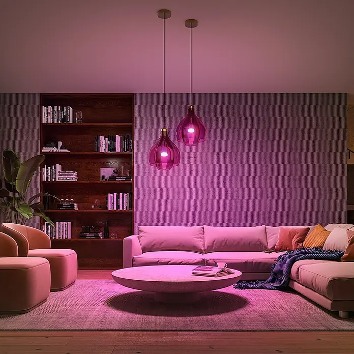 Philips Hue Smart-LED-Lampe Set mit Dimmcontroller, Steuerzentrale - E27, Dimmbar, RGBW, 2 Stk. - Zwei stilvolle Pendelleuchten in Pink hängen über einem modernen Wohnzimmer mit Sofa, Couchtisch und Bücherregal. Sie strahlen ein warmes, einladendes Licht aus.