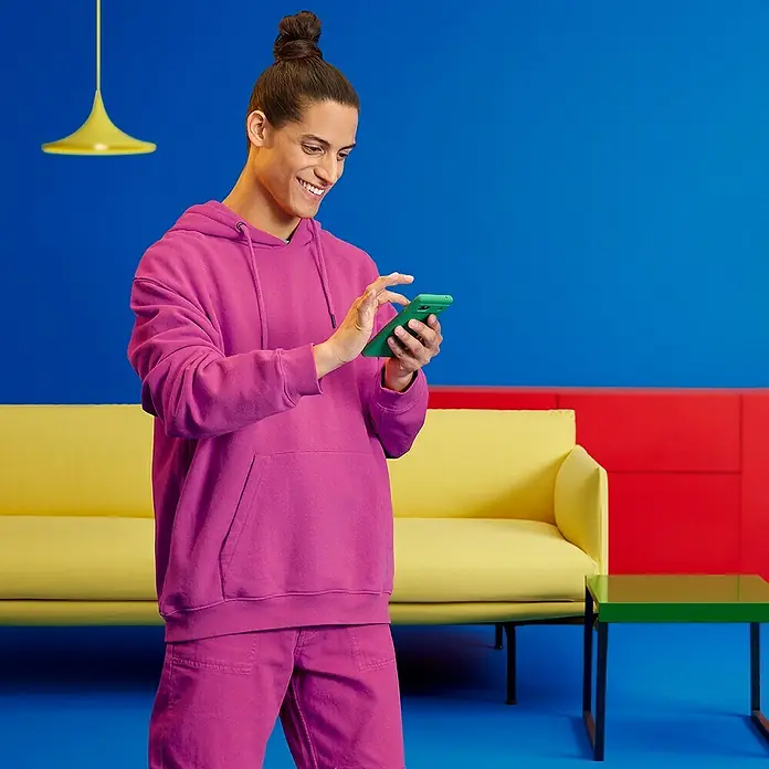 Philips Wiz Smart-LED-Lampe matter - E27, Dimmbar, RGBW, 806 lm, 8,5 W, 2 Stk. - Der Mann trägt einen auffälligen, pinkfarbenen Hoodie und passende Hosen, während er auf sein grünes Smartphone schaut. Ein moderner, farbenfroher Look.