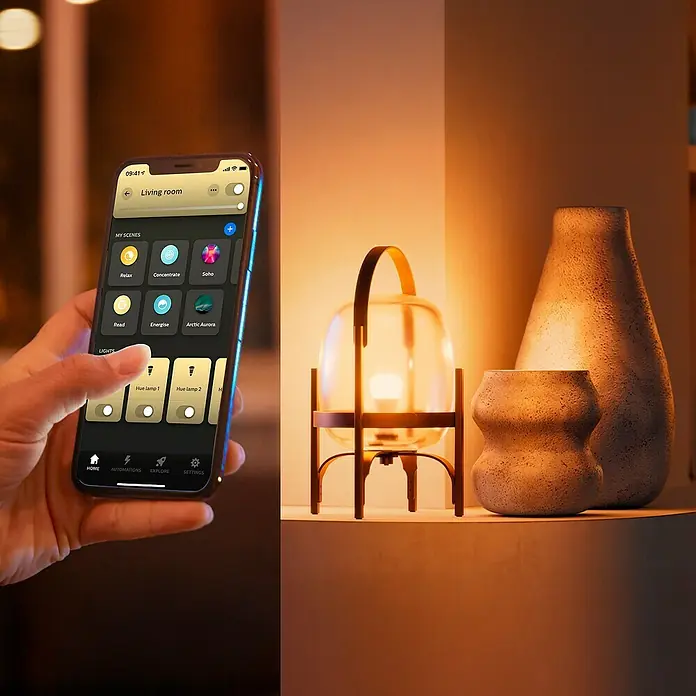 Philips Hue Smart-LED-Lampe White Ambiance 1600 matter - E27, Dimmbar, Kaltweiß, 1.600 lm, 11,8 W - Nahaufnahme eines Smartphones mit einer App zur Steuerung einer Philips Hue Lampe, die neben dekorativen Vasen auf einem Regal steht.