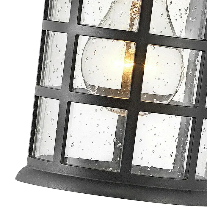 Elstead Außenwandleuchte Freeport - 60 W, 18,5 x 23,8 x 23,8 cm, Schwarz, IP44 - Nahaufnahme einer Außenleuchte mit schwarzen Akzenten und klarem, blasigem Glas, die ein warmes Licht ausstrahlt.