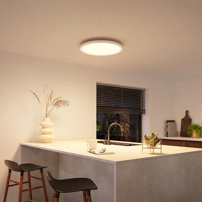 Philips Hue LED-Panel rund White & Color Ambiance Surimu - 60 W, Weiß, Opal, RGBW - Eine runde Deckenleuchte mit weißem Rand, die ein warmes, helles Licht spendet und eine moderne Küche beleuchtet.