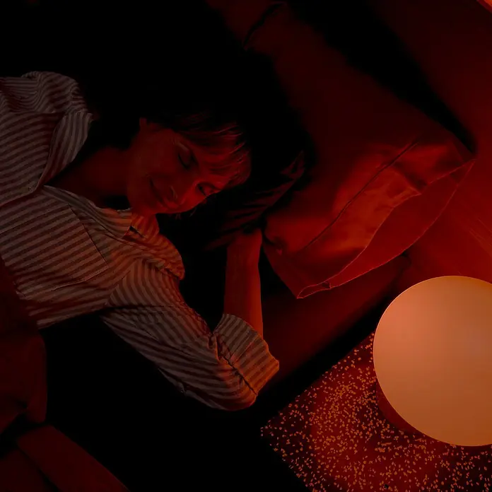 Philips Wiz Smart-LED-Lampe - E27, Dimmbar, RGBW, 12,3 W, 1 Stk. - Frau schläft friedlich im Bett mit entspannendem Ambiente-Lichtschein der Nachttischlampe für eine ruhige Nachtruhe.