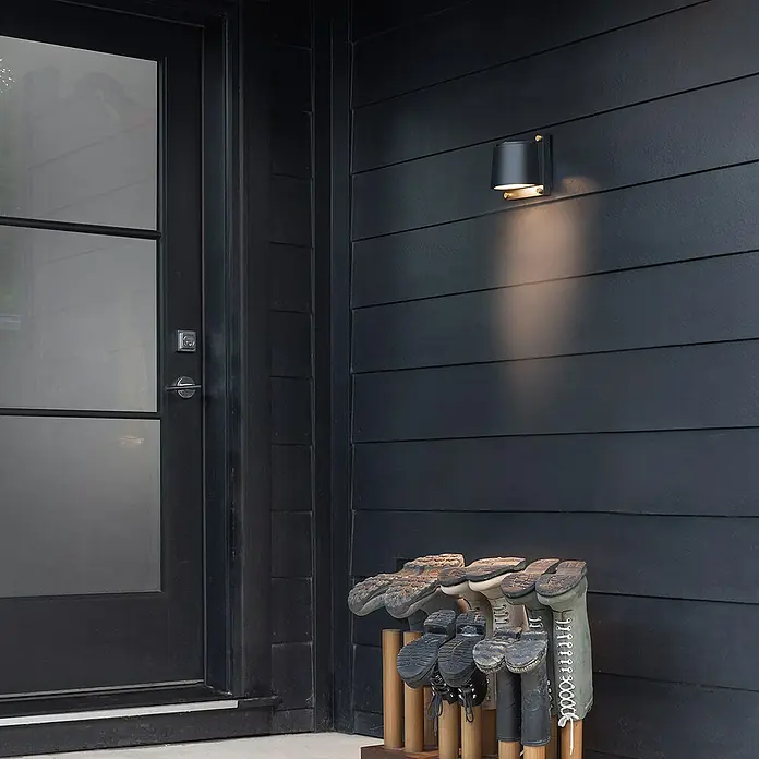 Elstead LED-Außenwandleuchte Scout - 7 W, 12 x 16,5 x 16,5 cm, Black, IP44 - Eine elegante Außenwandleuchte in Schwarz mit warmem Lichtschein neben einer Haustür und einem Schuhständer.