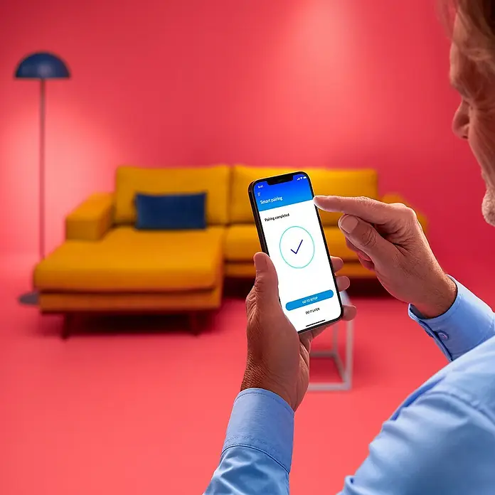 Philips Wiz Smart-LED-Lampe - E27, Dimmbar, RGBW, 18,5 W, 1 Stk. - Ein Mann nutzt eine App mit der Meldung "Kopplung abgeschlossen" auf seinem Smartphone, um Geräte zu verbinden.