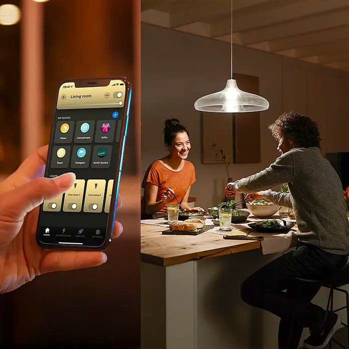 Philips Hue Smart-LED-Lampen Set White 1100 matter - E27, Dimmbar, Warmweiß, 1.100 lm, 9,5 W, 2 Stk. - Intelligente Beleuchtung im Esszimmer: Ein Smartphone steuert die Philips Hue Lampe über eine App, während ein Paar zu Abend isst.