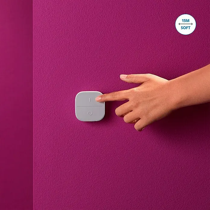 Philips Wiz Fernbedienung smarter Connected Button - Weiß - Nahaufnahme einer Hand, die einen grauen, quadratischen Lichtschalter an einer violetten Wand drückt.