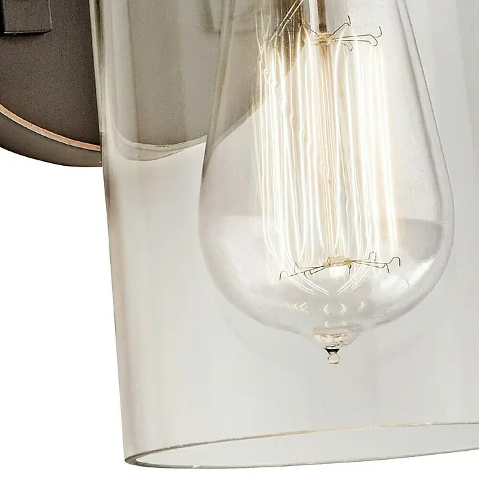 Elstead Wandleuchte Brinley - 60 W, L x B x H: 15,9 x 12,7 x 29,2 cm, Altbronze, E27 - Nahaufnahme einer Wandleuchte mit Edison-Glühbirne in einem klaren Glaszylinder, die ein warmes, einladendes Licht ausstrahlt.