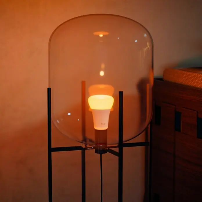 Philips Hue Smart-LED-Lampe White and Color 1600 matter - E27, Dimmbar, RGB, 1.600 lm, 11,8 W - Nahaufnahme einer modernen Stehlampe mit einem durchsichtigen, länglichen Lampenschirm und warmem Licht.