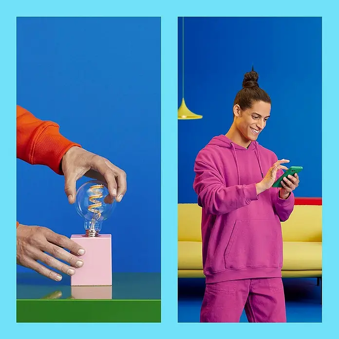 Philips Wiz Smart-LED-Lampe - E27, Dimmbar, RGBW, 470 lm, 6,3 W, 1 Stk., A60 - Stylische LED-Glühbirne auf einem rosa Sockel, kombiniert mit einem Mann im trendigen Hoodie mit Handy.